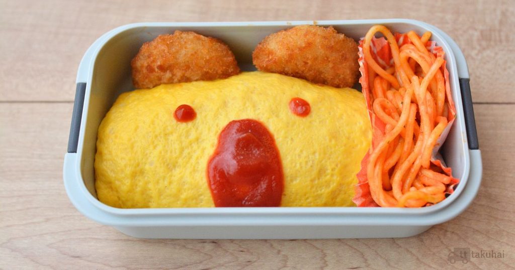 オムライスにケチャップで顔を描き、揚げ物とナポリタンを詰めたお弁当
